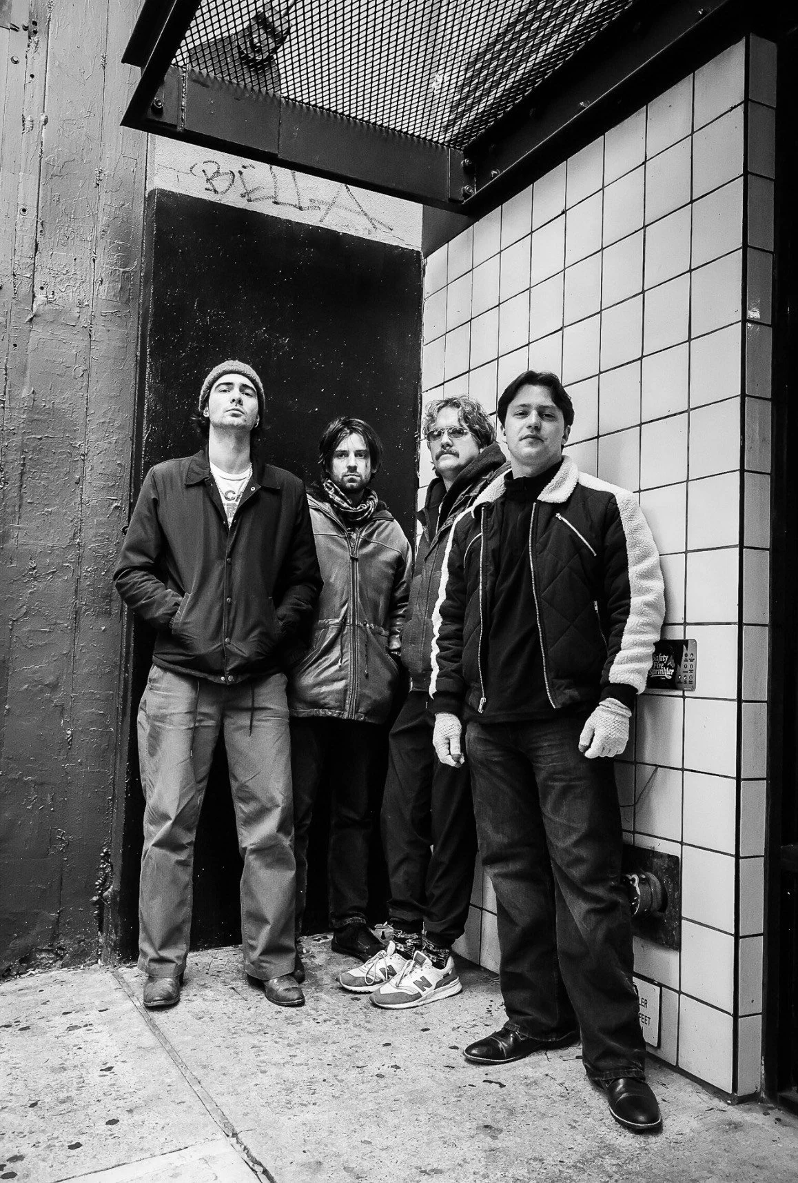 Four men standing against a wall on a city sidewalk, black and white photo.