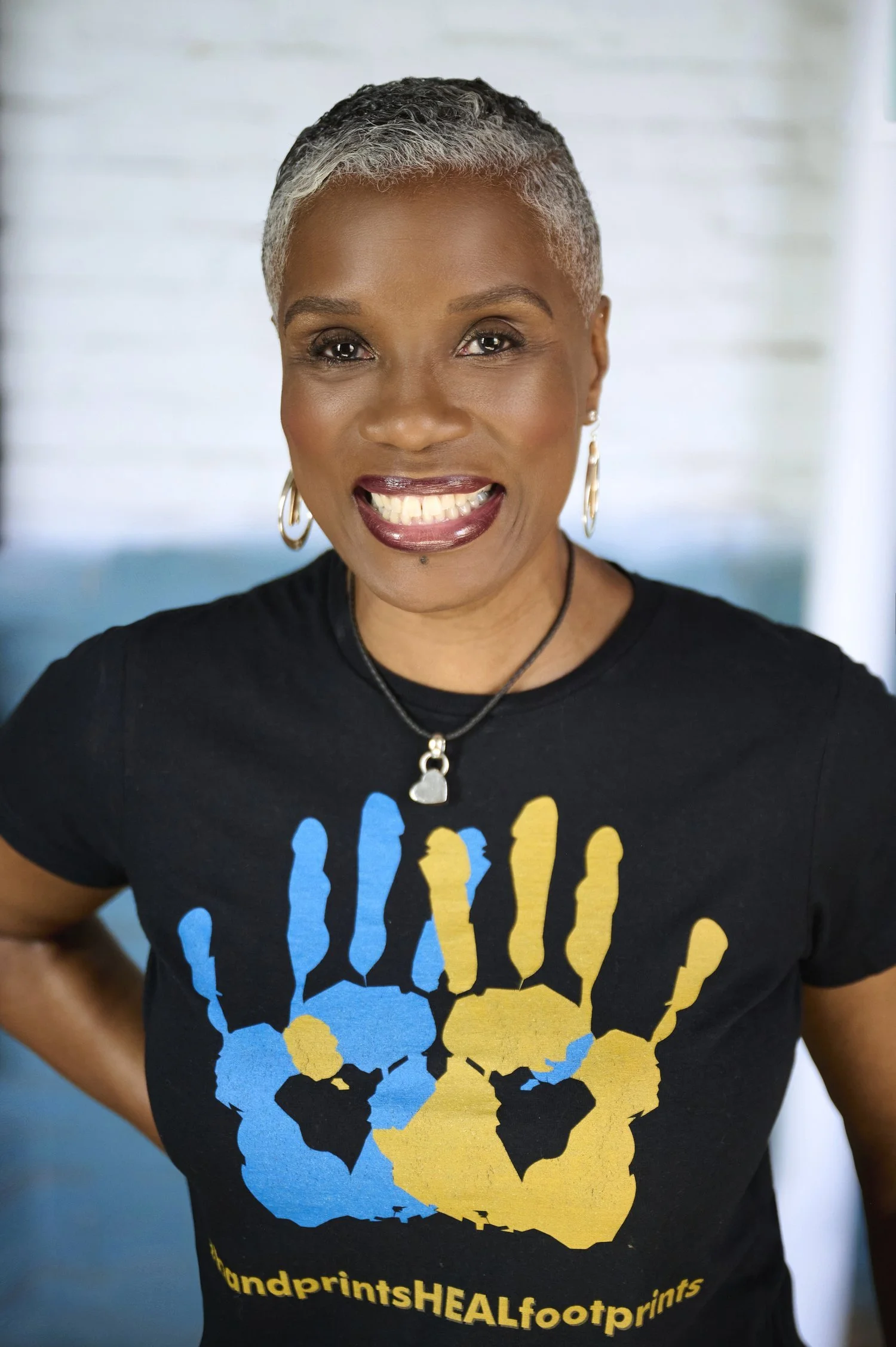 Dr. Christine Herring smiling in a black t-shirt with blue and yellow handprints, representing her role as Founder and CEO of Herring Seminars & Consulting, specializing in communication and leadership development.