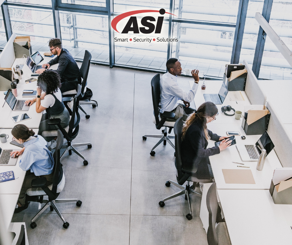 Office workspace with four employees working at desks, using laptops and tablets, with a logo that says ASI and the words 'Smart Security Solutions' in the background.