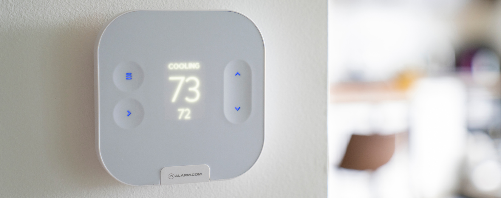 Smart thermostat displaying a current temperature of 73 degrees Fahrenheit in cooling mode, mounted on a beige wall
