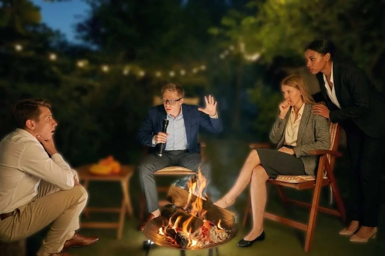 Colleagues wearing professional clothing tell stories around campfire.