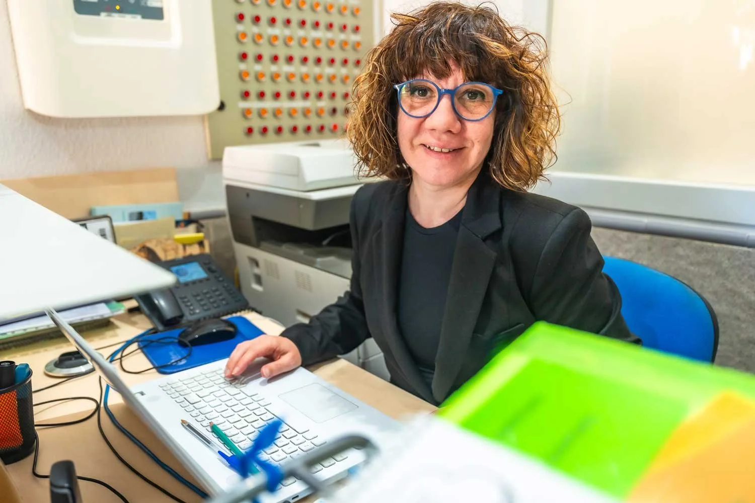 A frazzled administrative office worker looks up from her equipment-laden desk