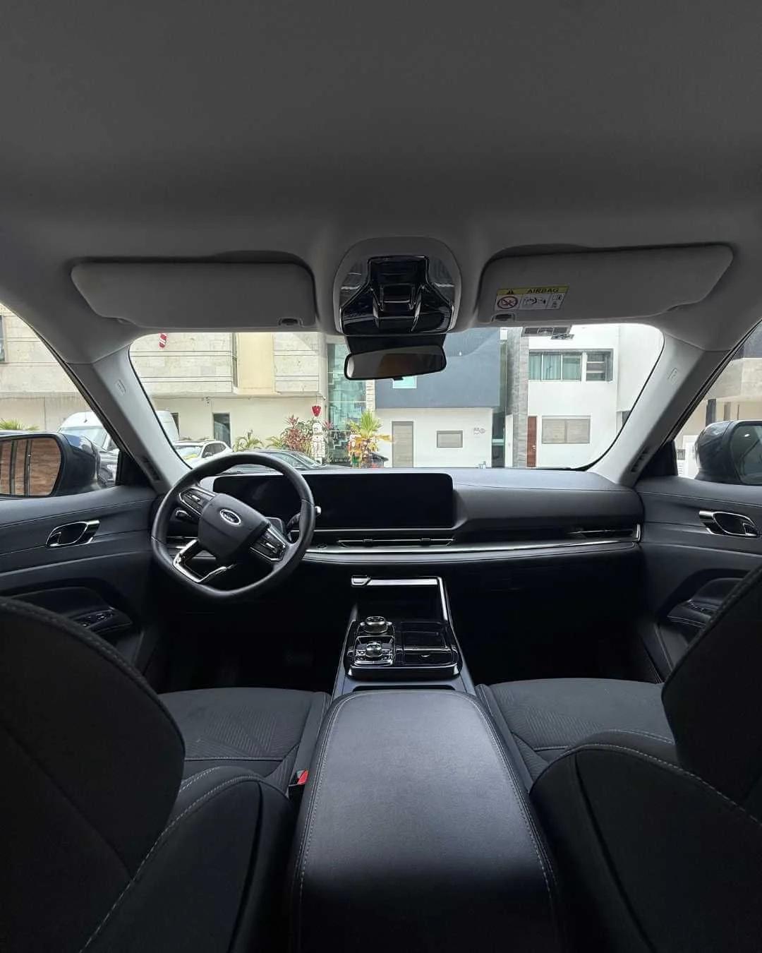 Interior de un automóvil moderno desde la perspectiva del asiento trasero, con volante, tablero digital grande y consola central con controles.