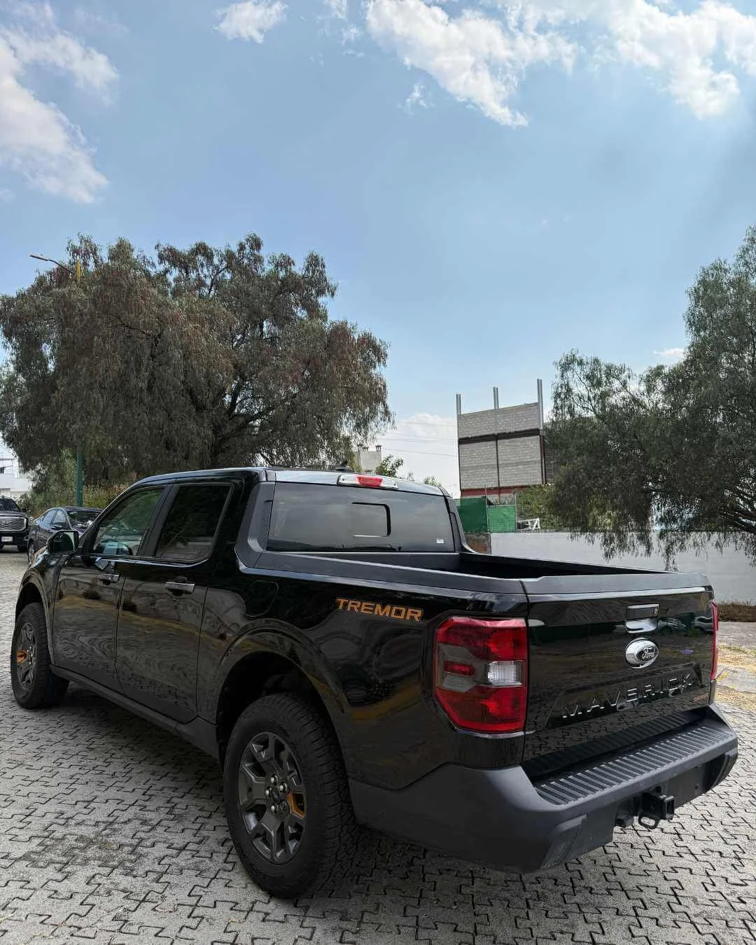 Camioneta Ford Maverick negra en un estacionamiento, con árboles y cielo azul en el fondo.