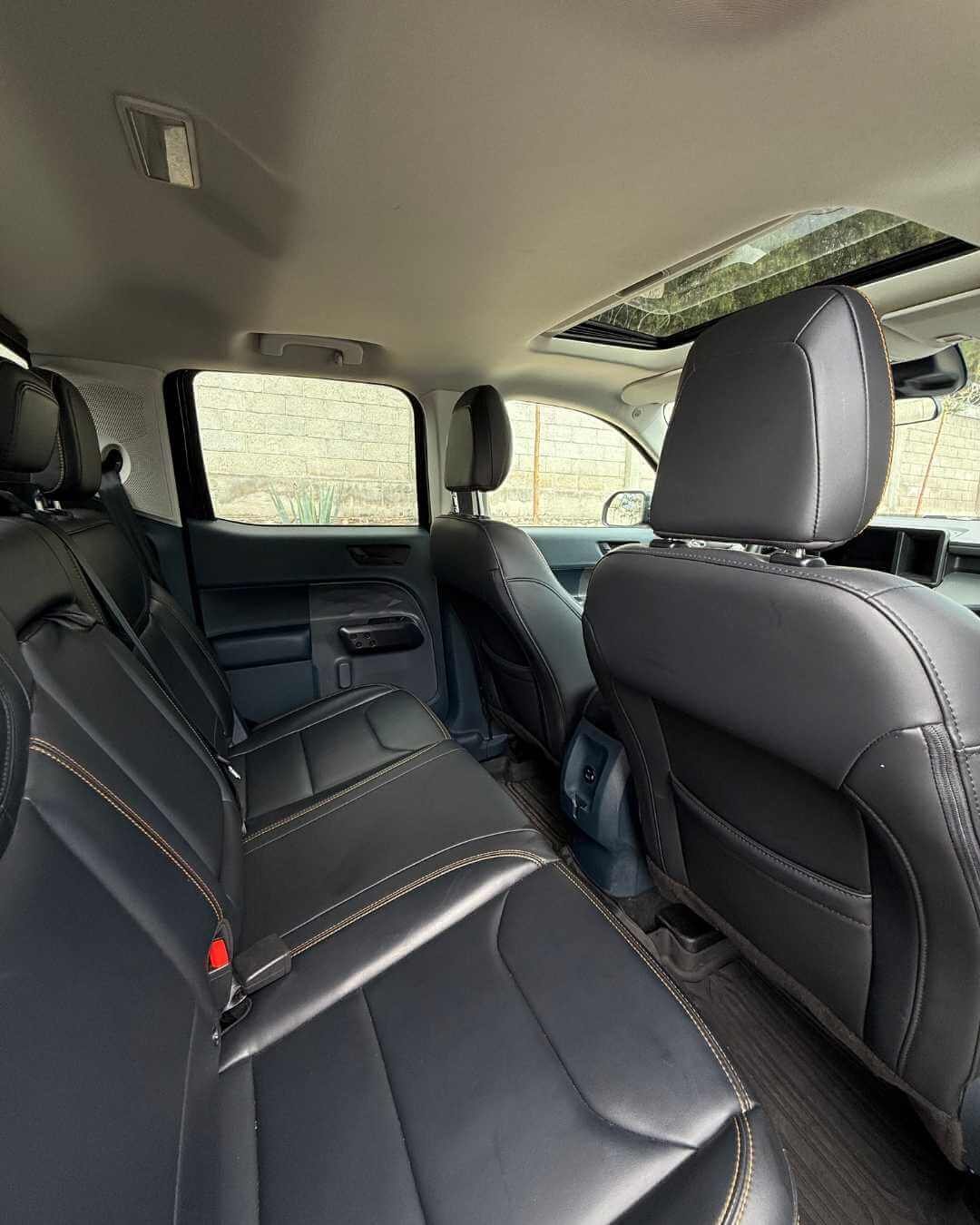 Interior de coche con asientos de cuero negro, ventanas laterales y techo con cielo raso, vista desde la parte trasera hacia adelante.