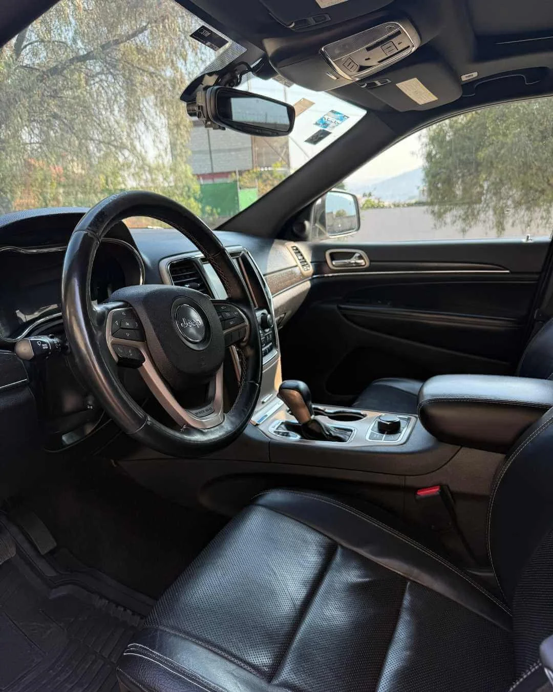 Interior de un vehículo SUV Jeep, con volante, tablero, consola central con control giratorio y palanca de cambios, asiento de piel negra y espejo retrovisor con dispositivo de videovigilancia montado en el techo.