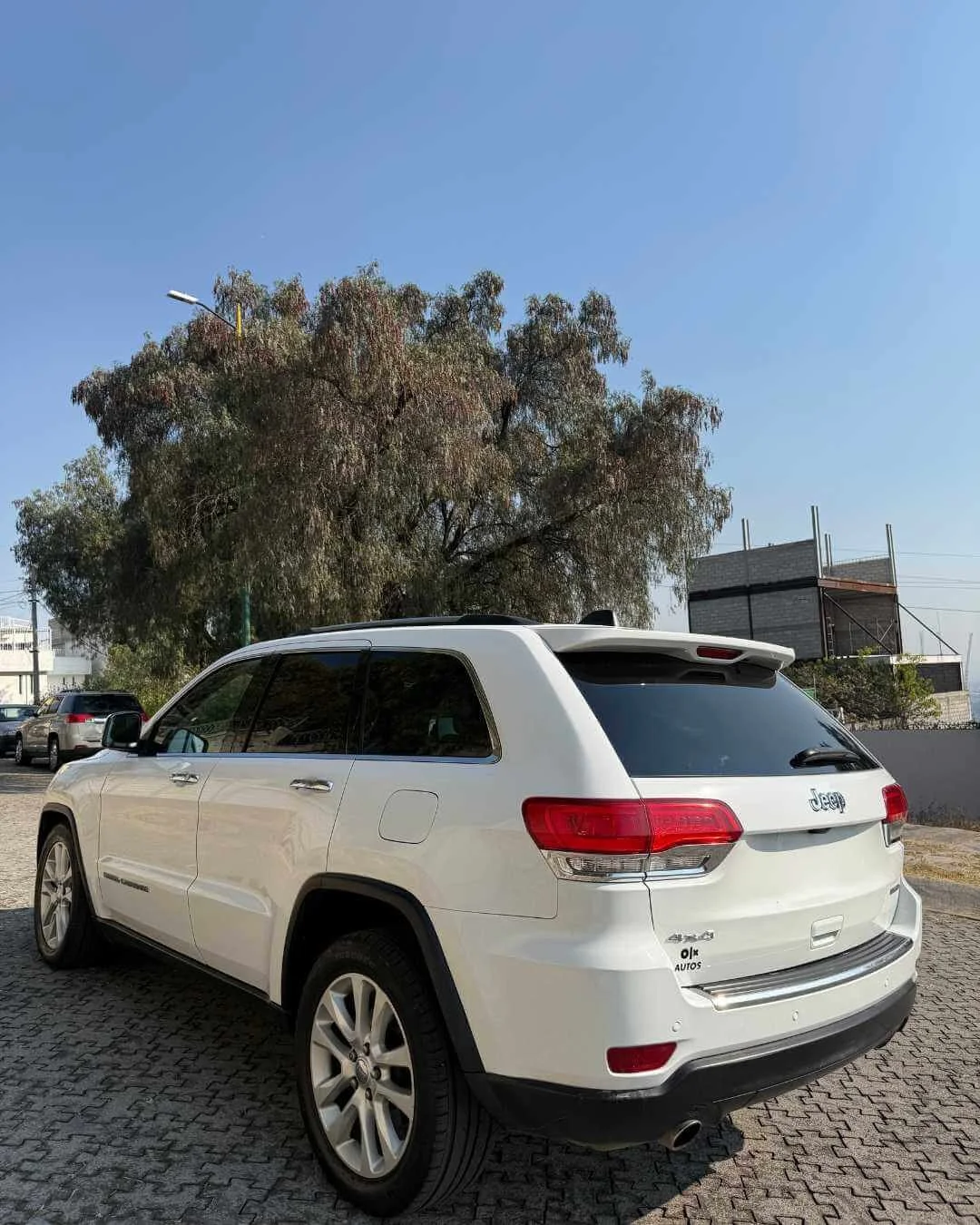 Auto Jeep color blanco estacionado en un lugar de grava, con árbol y cielo despejado al fondo.