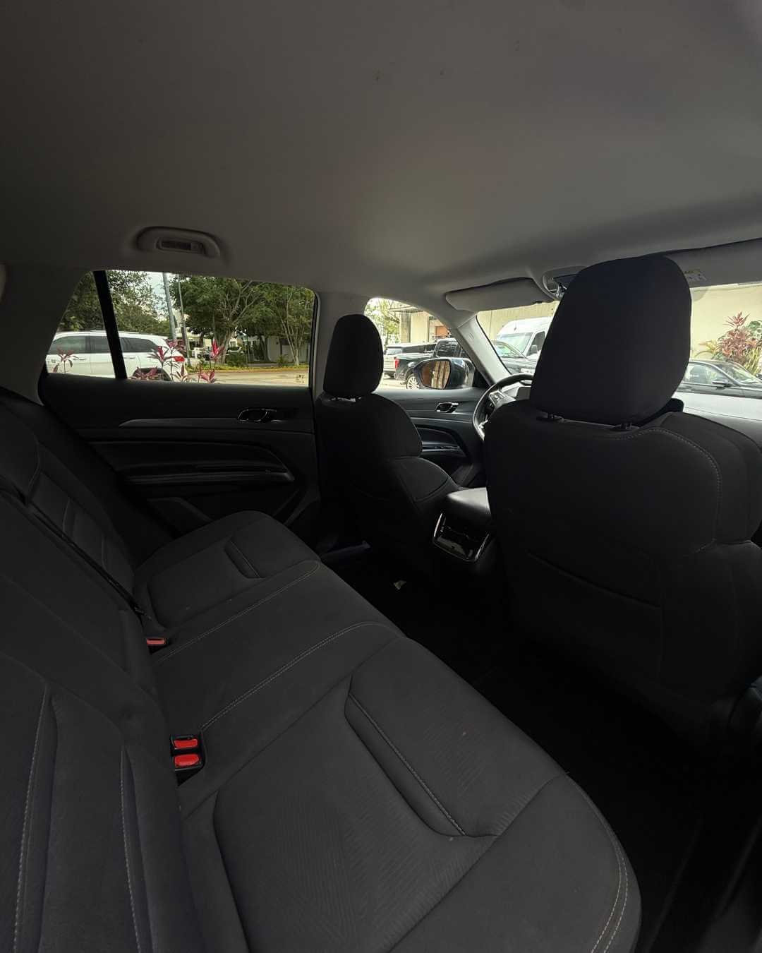 Interior de un automóvil con asientos negros, vista desde el asiento trasero hacia el conductor y el copiloto, con ventanas que muestran una calle y algunos autos afuera.