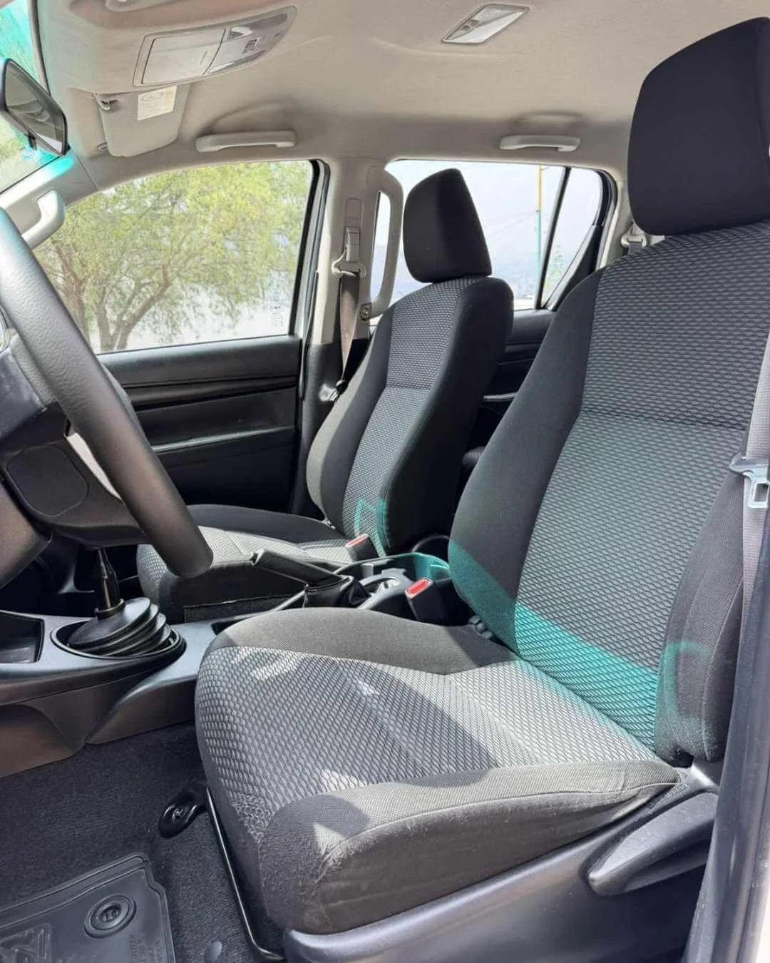 Interior de un vehículo, vista del asiento del conductor y del pasajero, volante, tablero y ventanas.
