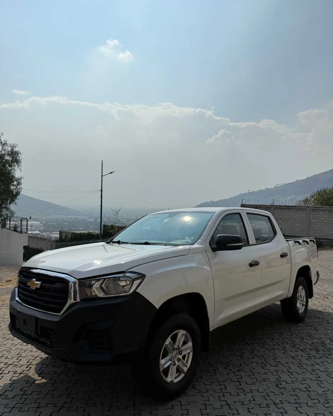 Camioneta Chevrolet blanca estacionada en un área al aire libre con montañas y cielo nublado de fondo.