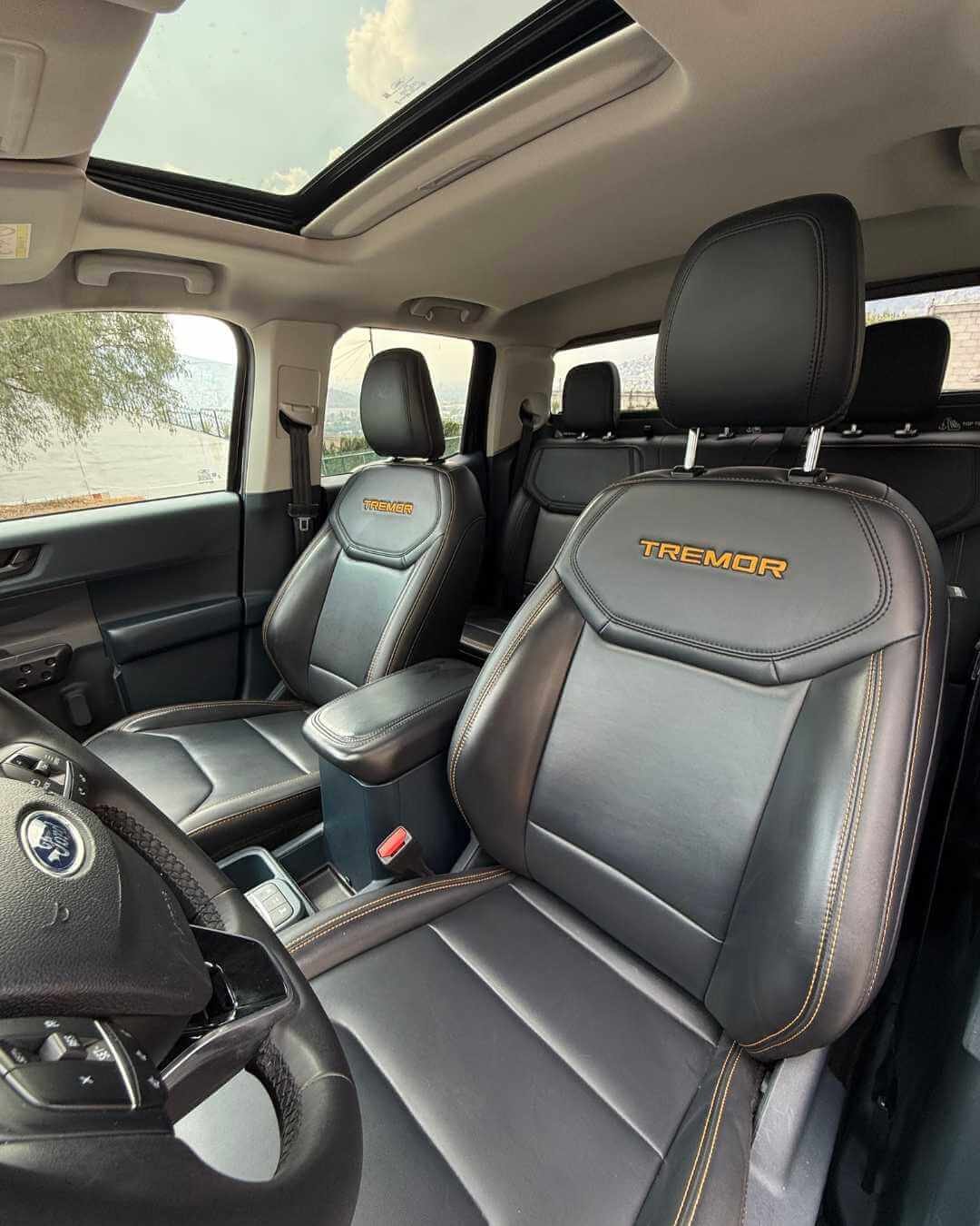 Interior de un vehículo, vista de los asientos de cuero negros con la marca 'Tremor' bordada en el respaldo, volante y cielo con techo de vidrio panorámico.