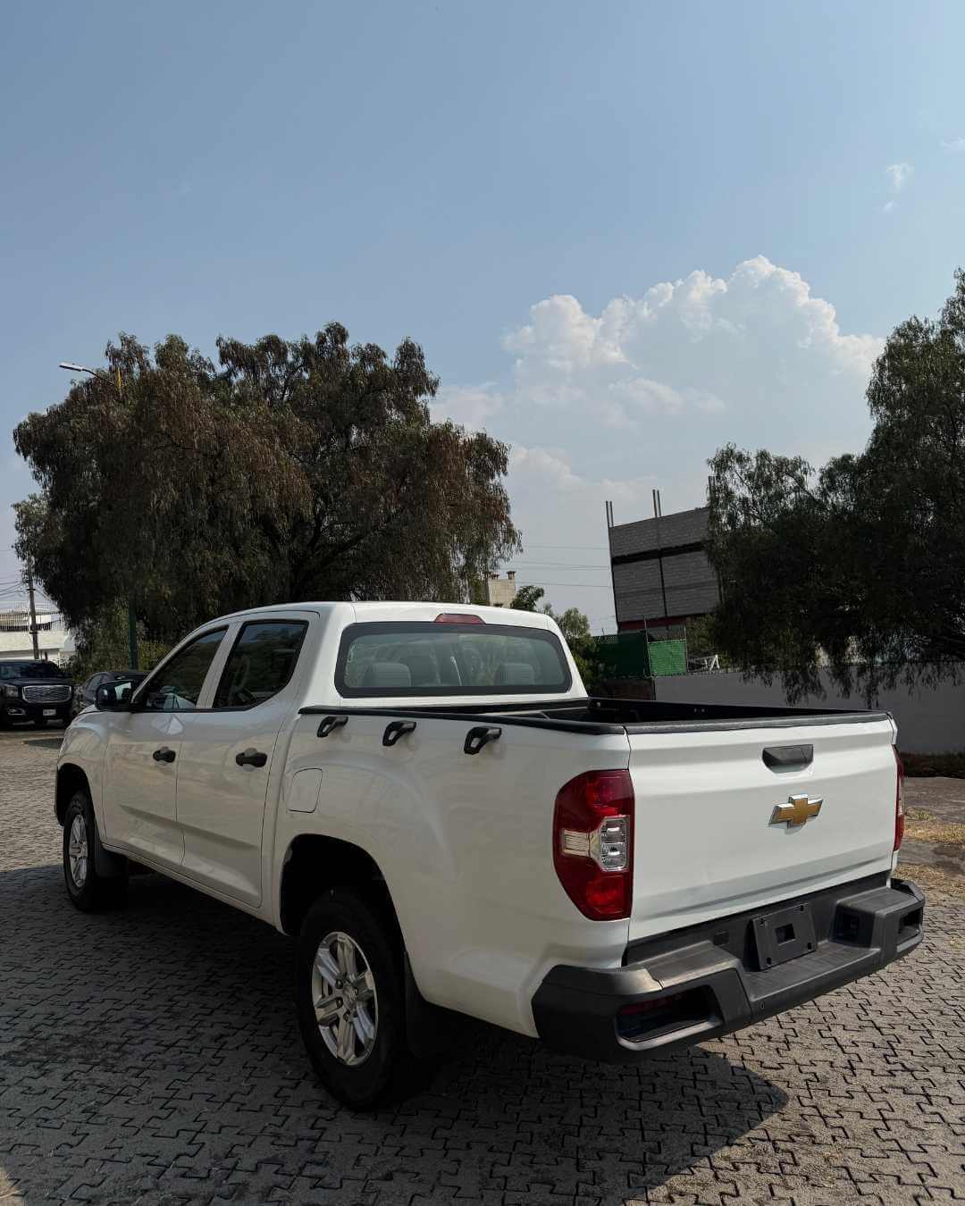 Camioneta blanca Chevrolet estacionada en un área pavimentada con árboles y cielo despejado.
