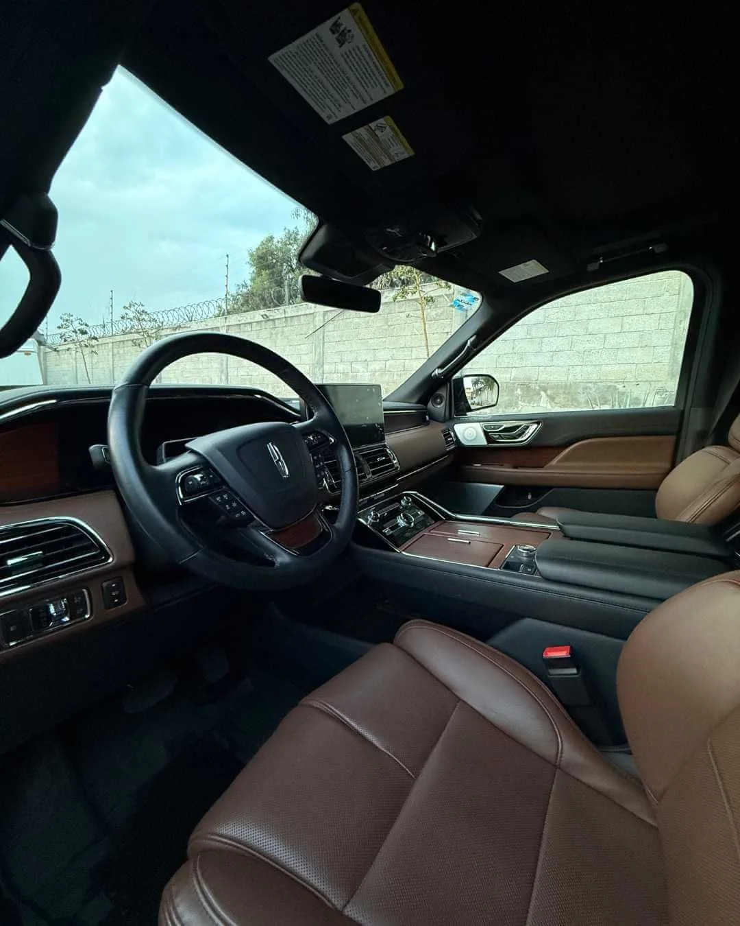 Interiores de un vehículo de lujo con volante, pantallas y asientos de cuero marrón.