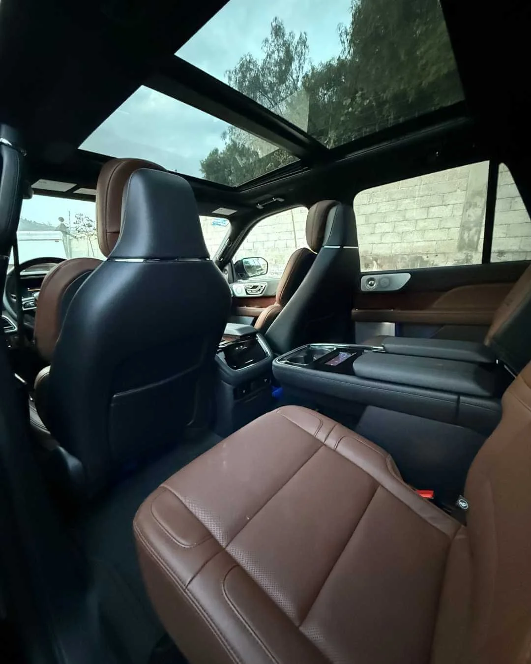 Interior de un vehículo con asientos de cuero marrón, techo de vidrio panorámico y consola central moderna.