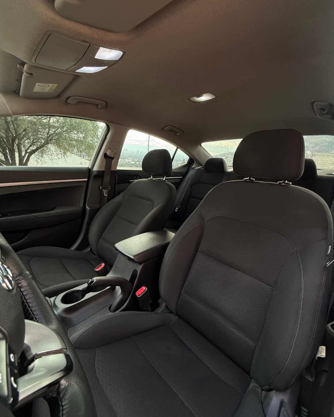 Interior de un coche, vista de los asientos delanteros y traseros, con ventanas que muestran un árbol y un paisaje de fondo.