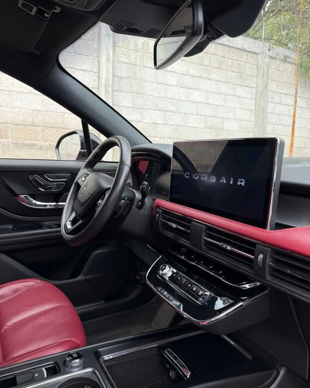 Interior de un automóvil con asientos y tablero en tonos negros y rojos, con una pantalla grande en el centro que muestra la marca 'CORSAIR'.
