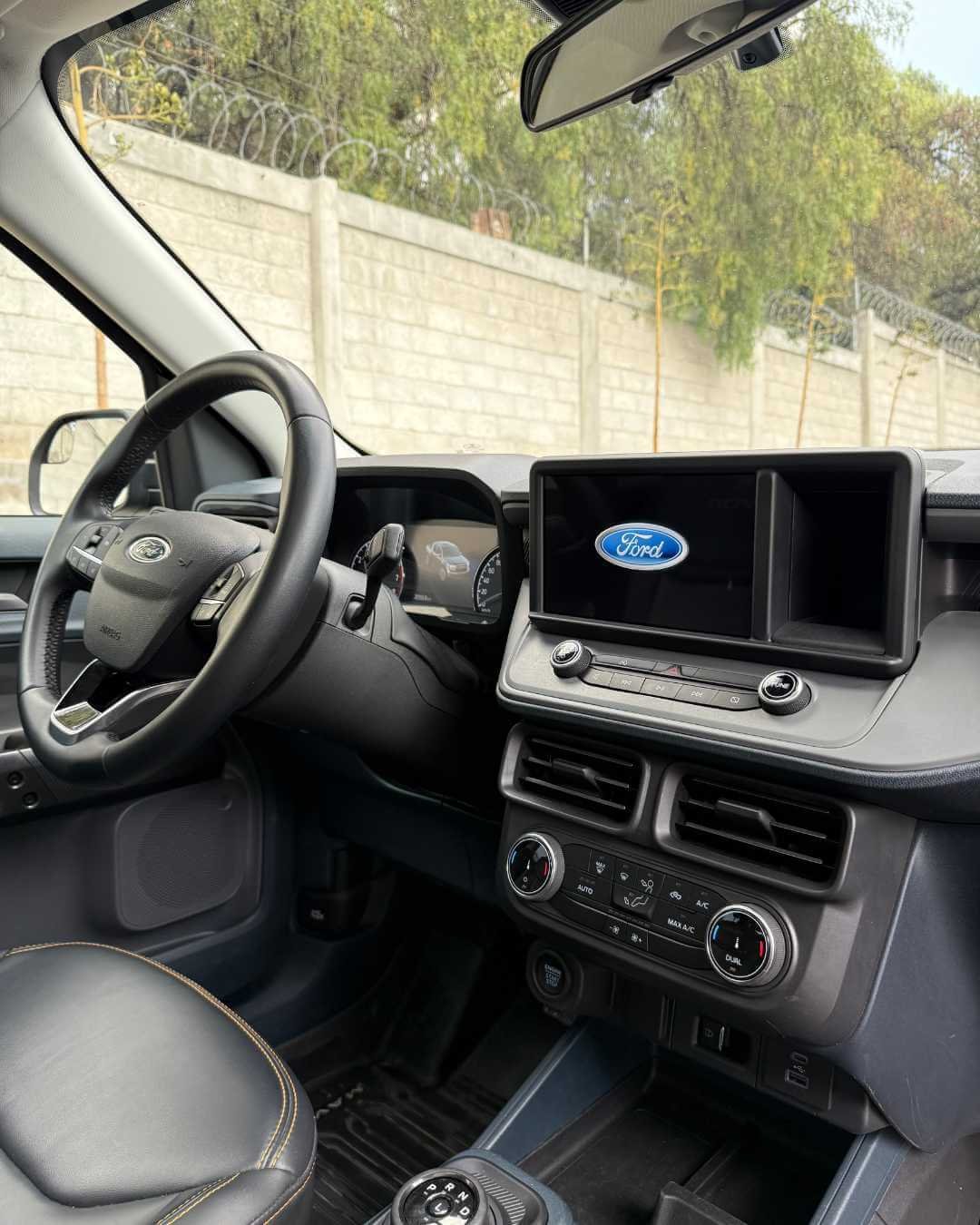 Interior de un vehículo Ford, mostrando el volante, consola central con pantalla y controles de clima.