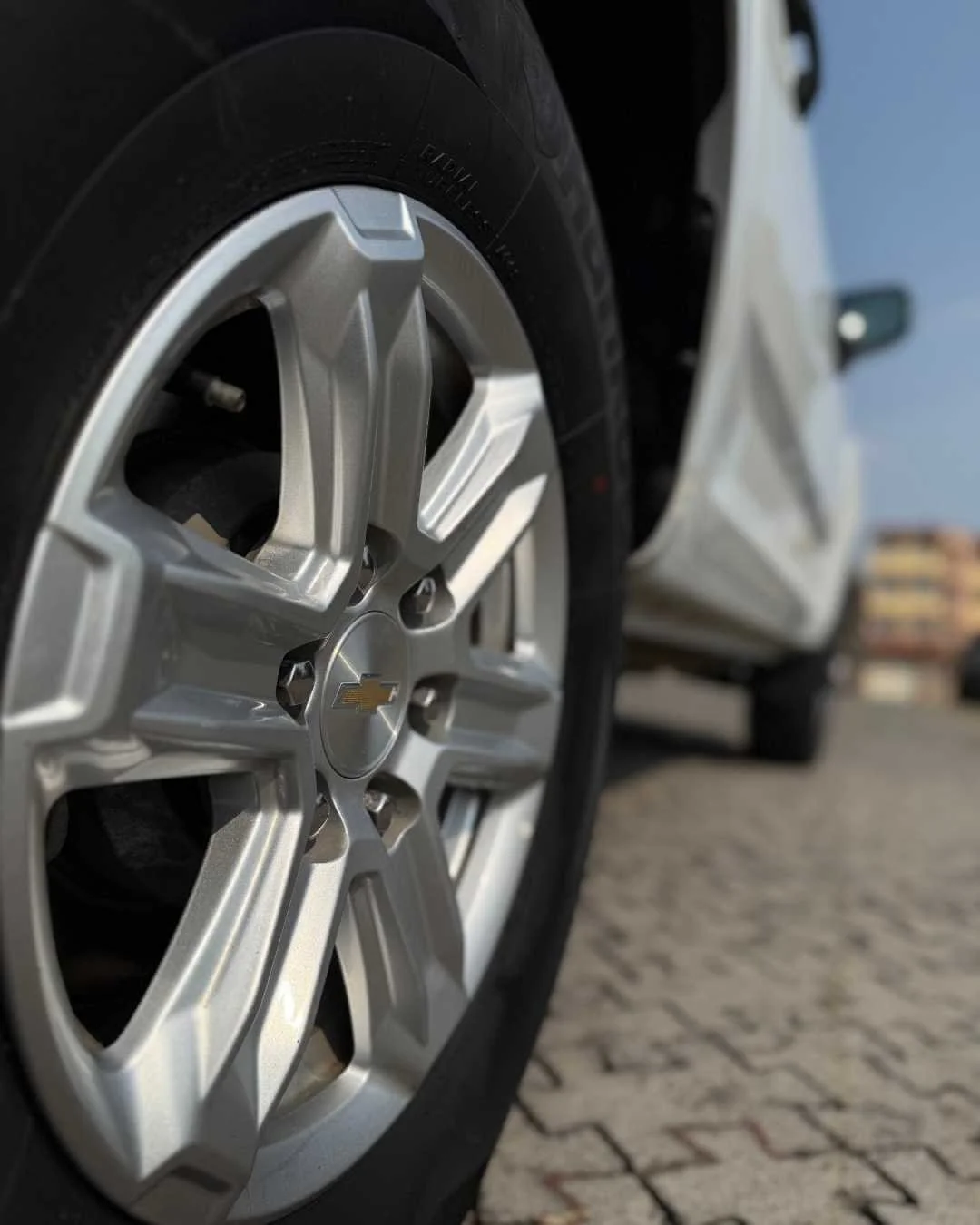 Rueda de automóvil con llanta Chevrolet en primer plano y fondo difuminado de otra parte del vehículo en el exterior.