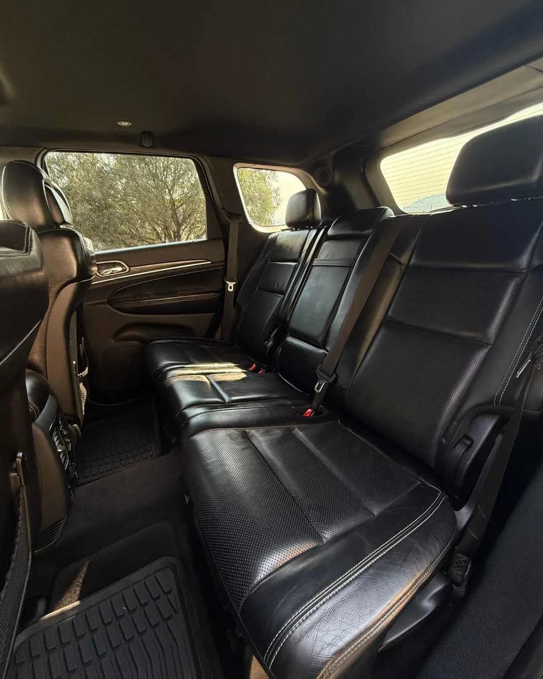 Asientos traseros de un vehículo con tapizado de cuero negro y ventanas con vista a árboles y cielo.