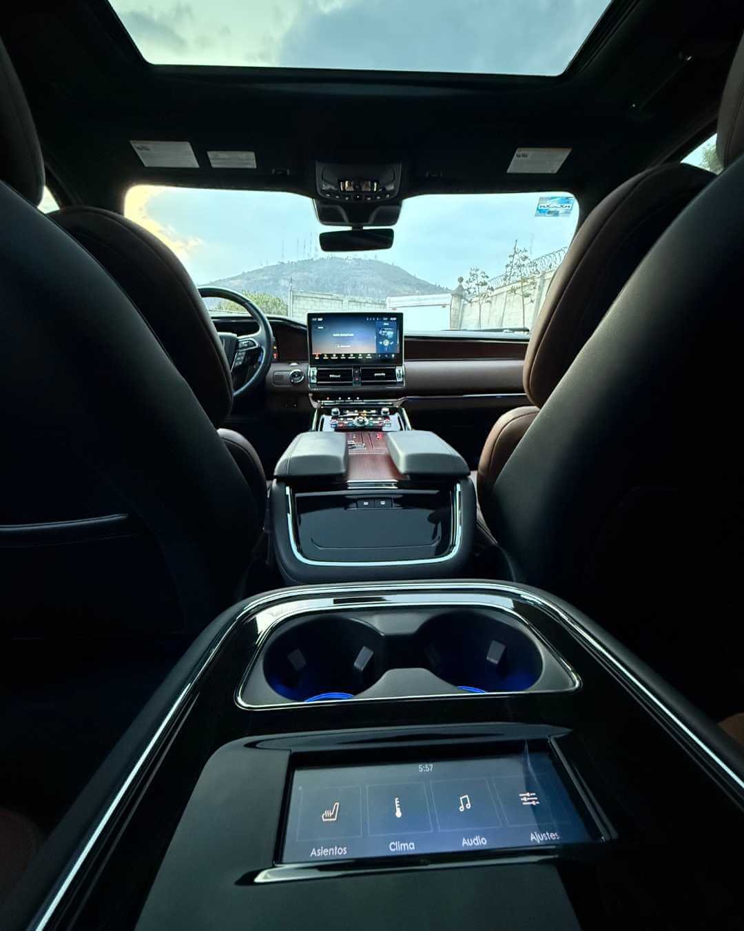 Interior de un coche de lujo con tablero digital, pantallas táctiles y ventanas panorámicas, viendo una montaña en el exterior.