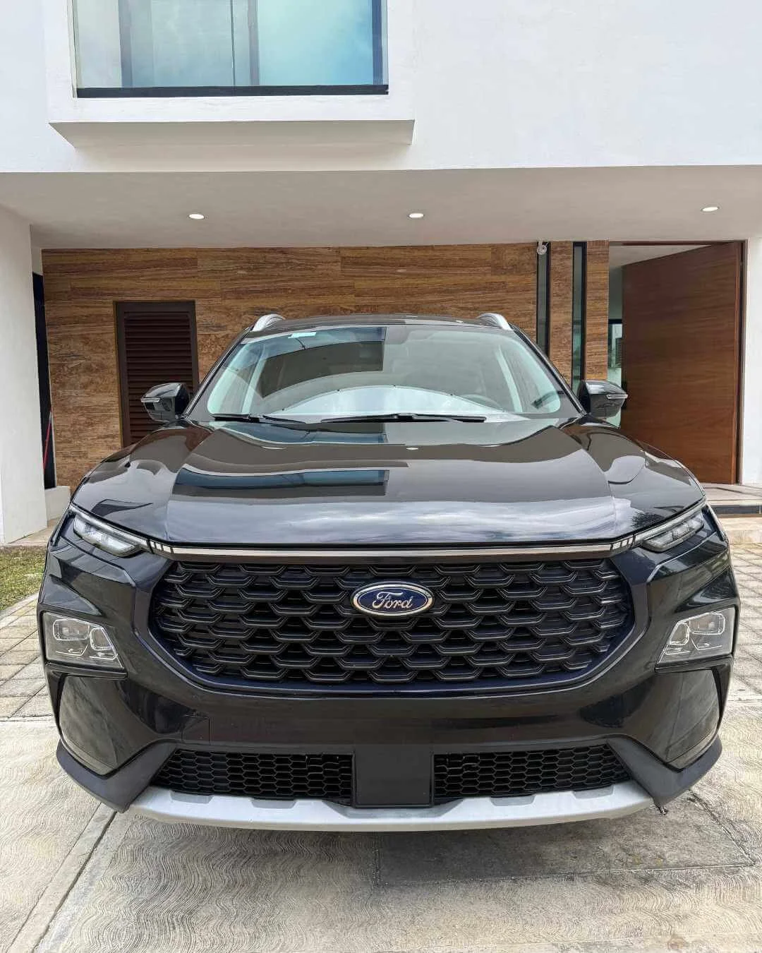 Auto Ford negro estacionado frente a una casa moderna con fachada de madera y paredes blancas.