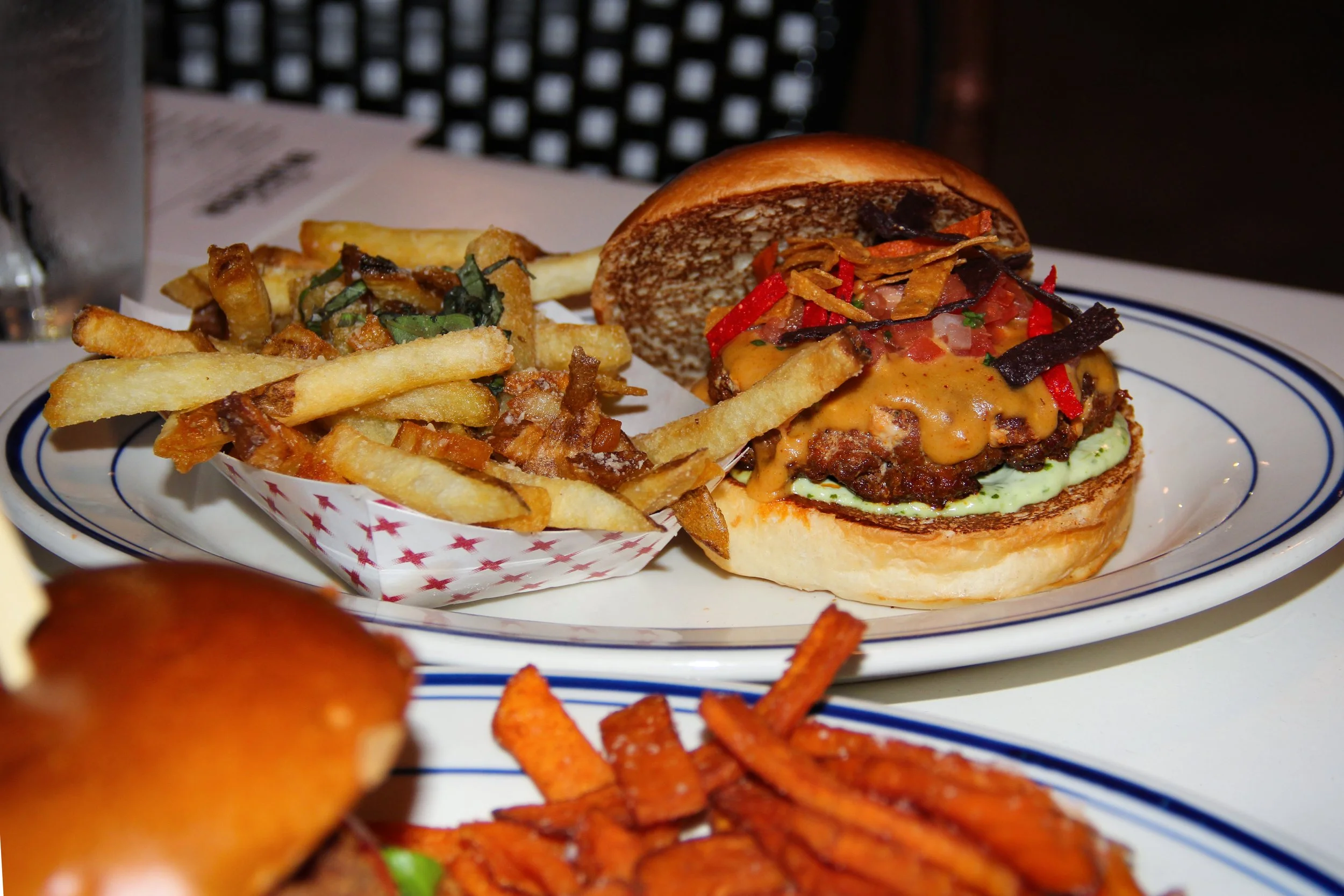 A plate with a cheeseburger with toppings, a side of French fries, and a second plate with sweet potato fries.