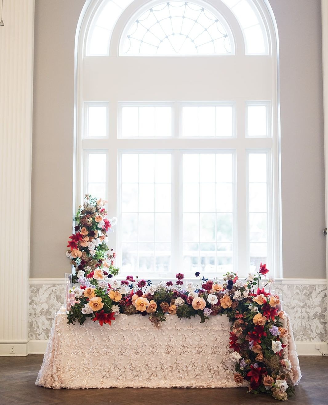 A seat for two, styled to stand out. This sweetheart table combined a textured linen with vibrant, cascading florals for a look that felt equal parts romantic and elevated. Tucked beneath soaring windows, it was the dreamiest little escape for just t