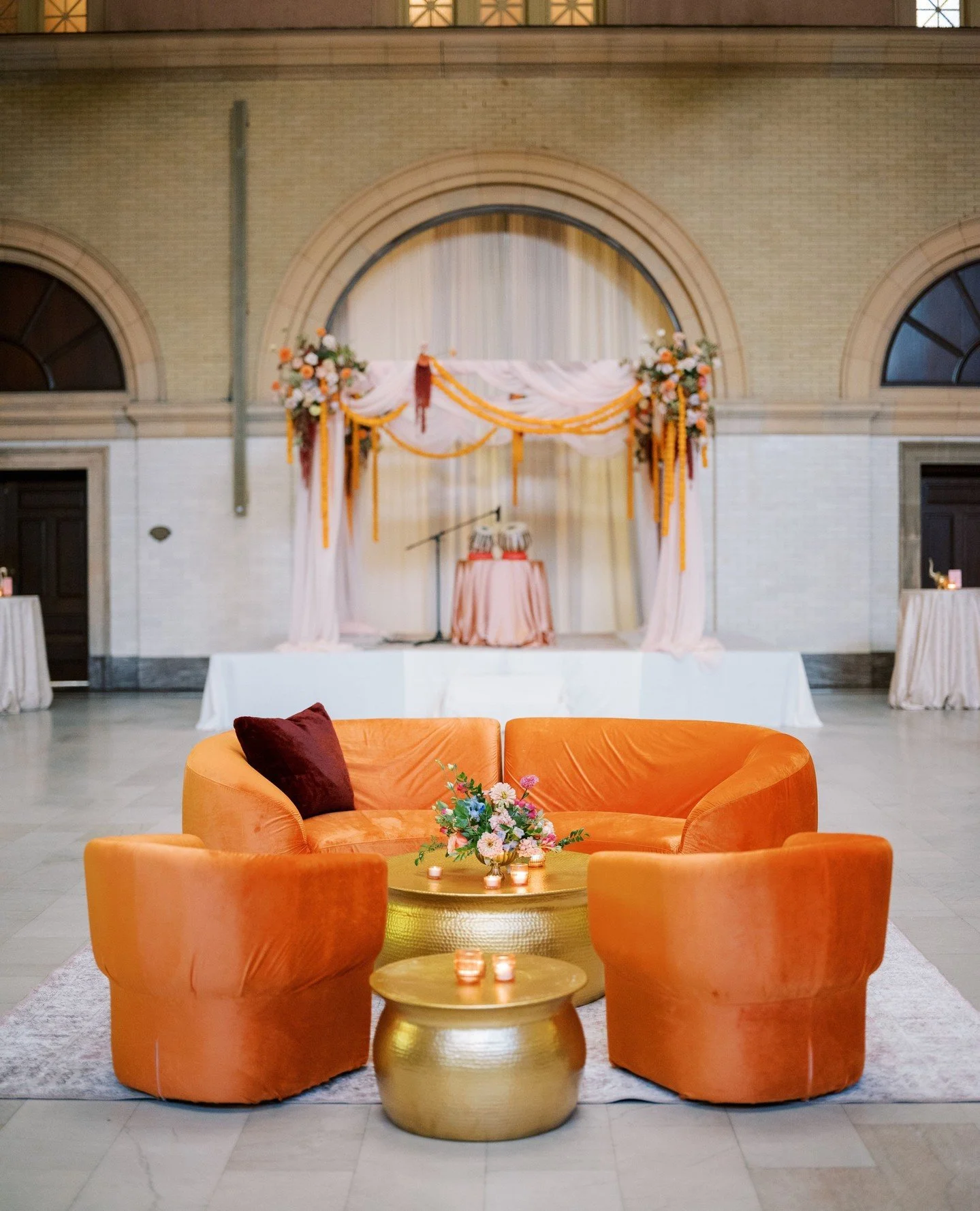 A repurposed mandap created the perfect backdrop for live music during cocktail hour. In the center of the room, a bold lounge grouping with orange velvet seating and gold tables added a striking pop of color.⁠
⁠
Planning | ⁠@stylearchitectsweddings⁠