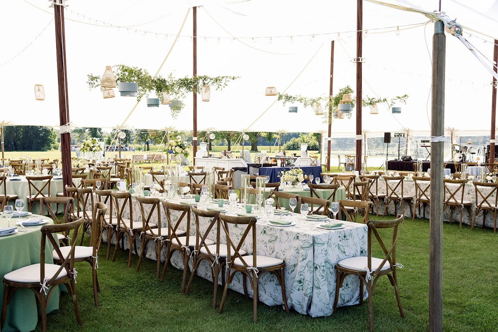 Wedding reception setup inside a large white tent with decorated tables, floral centerpieces, and wooden chairs.
