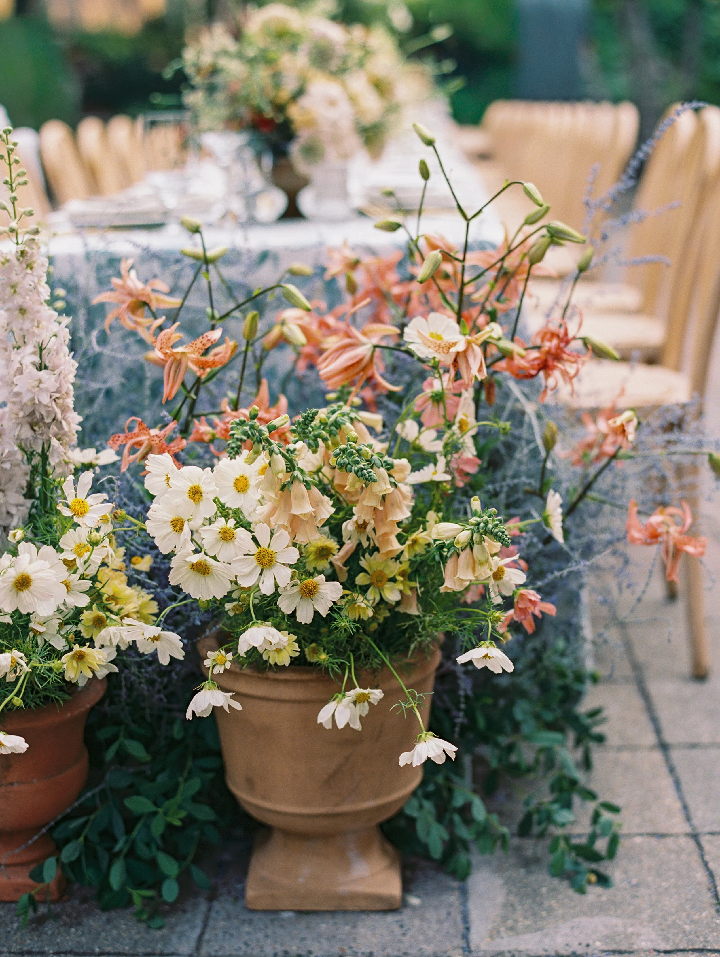 A floral centerpiece with white, pink, and purple flowers on a decorated outdoor dining table.