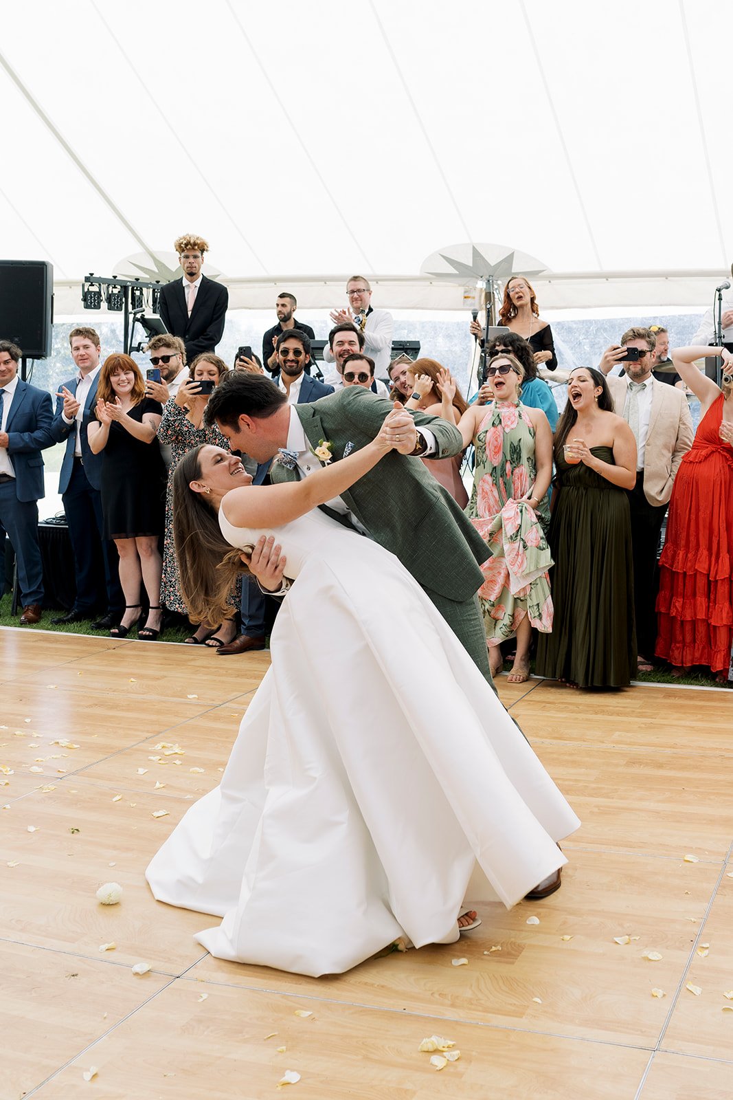 A couple dancing at their wedding reception, surrounded by friends and family inside a white tent.