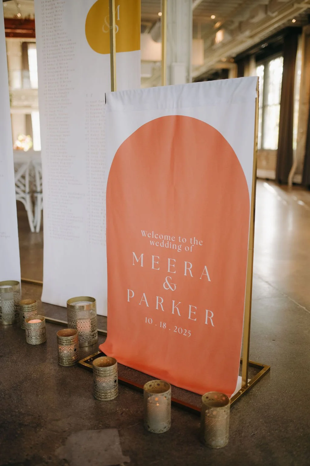 Wedding reception sign welcoming guests to the wedding of Meera and Parker on October 18, 2025, with candles in metallic holders surrounding the sign.