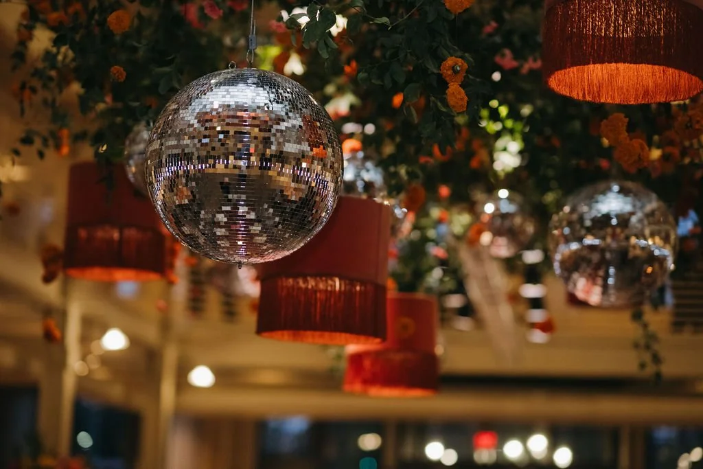 A disco ball hanging from the ceiling amidst hanging lamps and floral decorations.