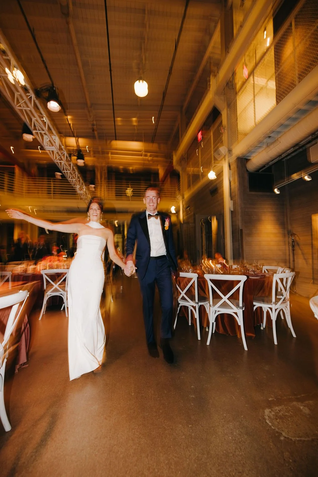A bride and groom holding hands and dancing in a warmly lit wedding reception hall.