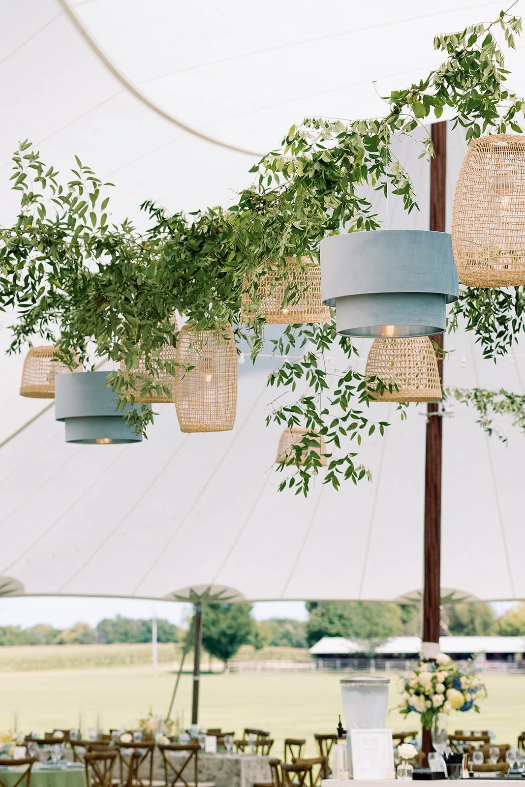 Decorative hanging lanterns and greenery inside a large tent at an outdoor event.
