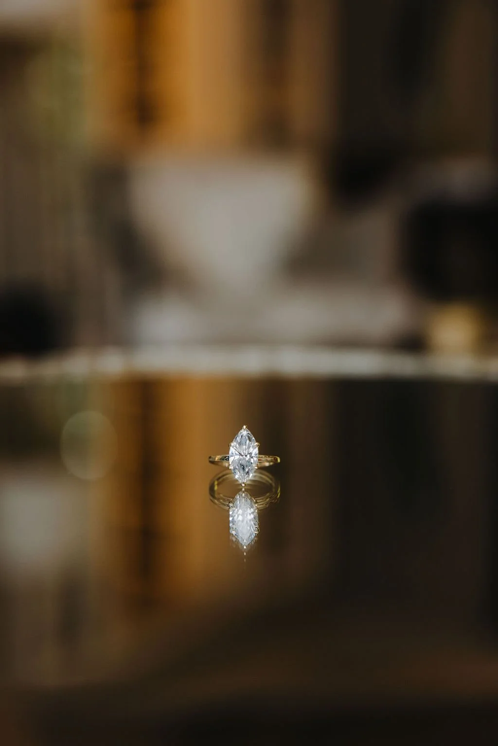 A diamond ring with a marquise-cut gemstone on a reflective surface, showing its reflection.