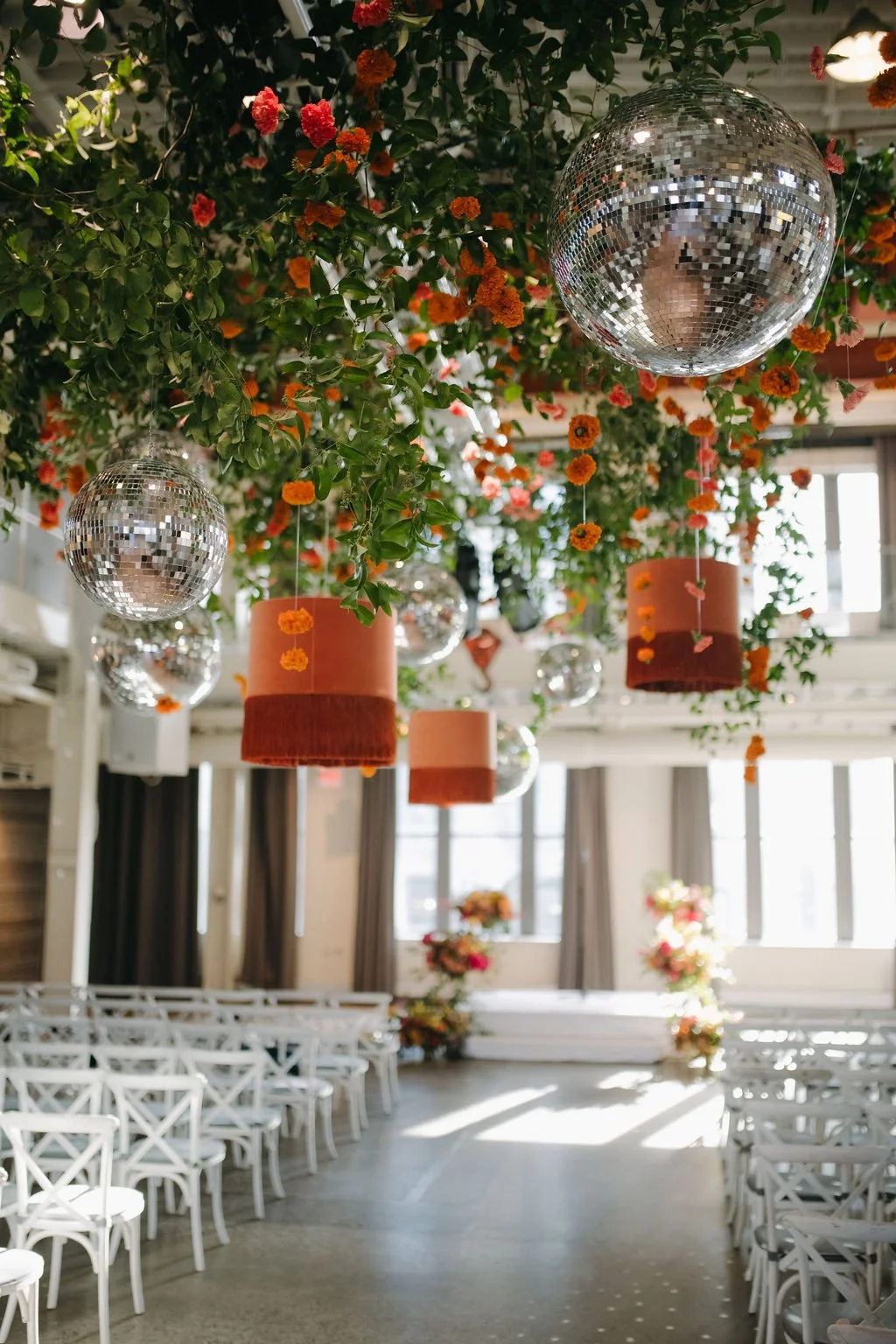 Indoor space decorated with hanging disco balls, orange flower lanterns, and lush greenery and flowers.