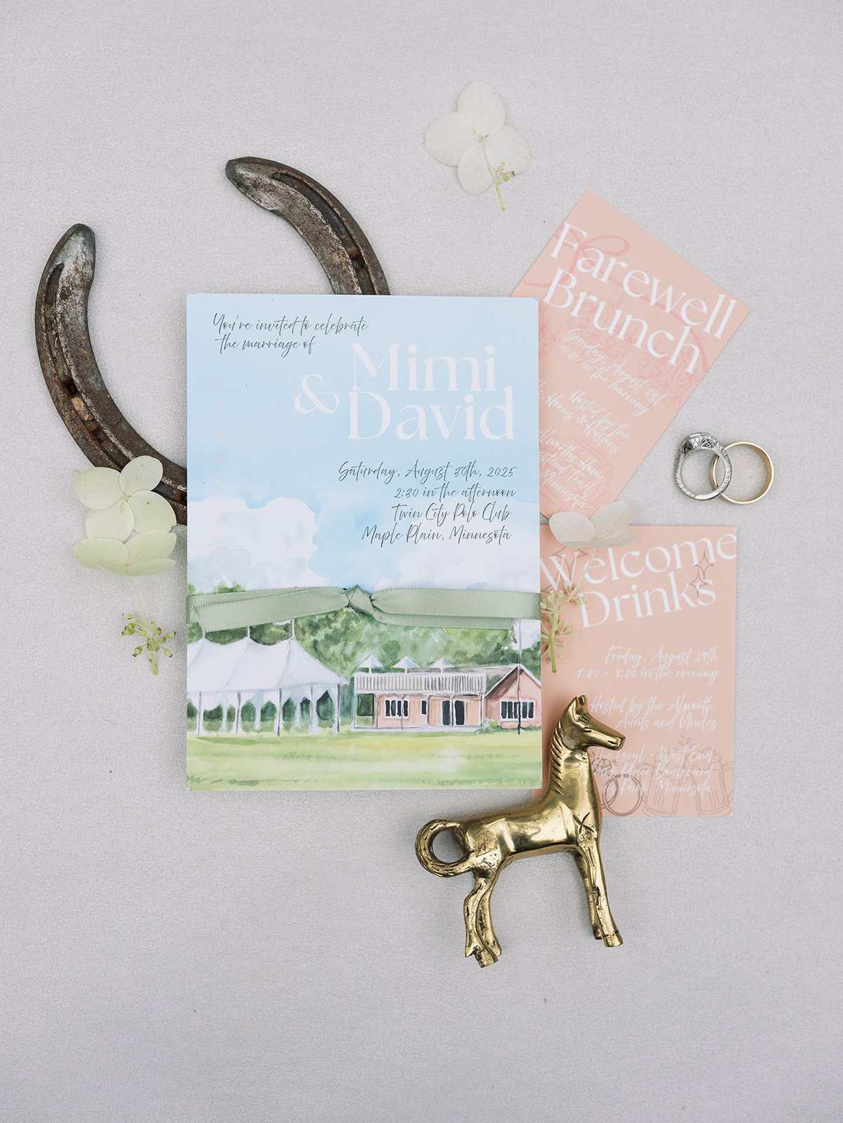 Wedding invitation and RSVP card with rings, horse figurine, horseshoes, and white flowers on a white background.