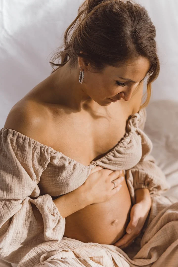 Een zwangere vrouw in een beige jurk die haar buik vasthoudt.