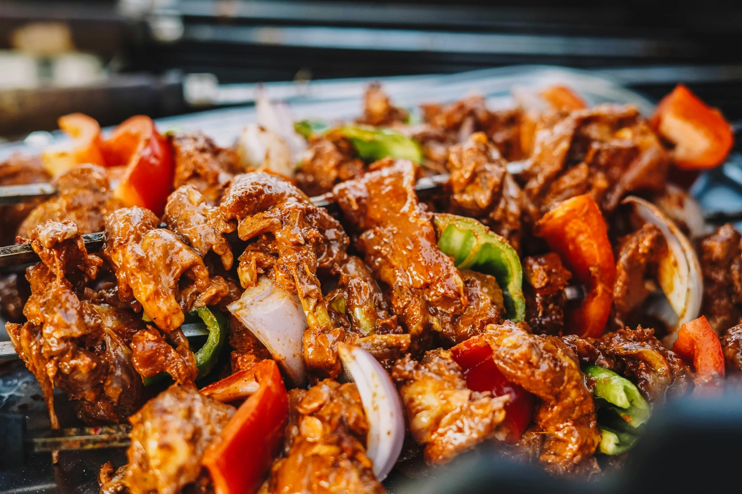 Close-up of marinated pieces of meat and vegetables, including red and green bell peppers and onions, skewered on a grill.
