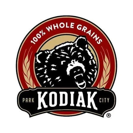 Logo with a bear's head, text '100% Whole Grains', and 'KODIAK' in bold, surrounded by a red and beige circular border.