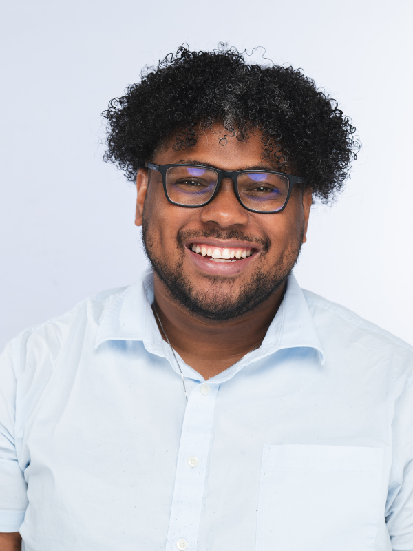 A smiling man with curly black hair, wearing glasses and a white button-up shirt.