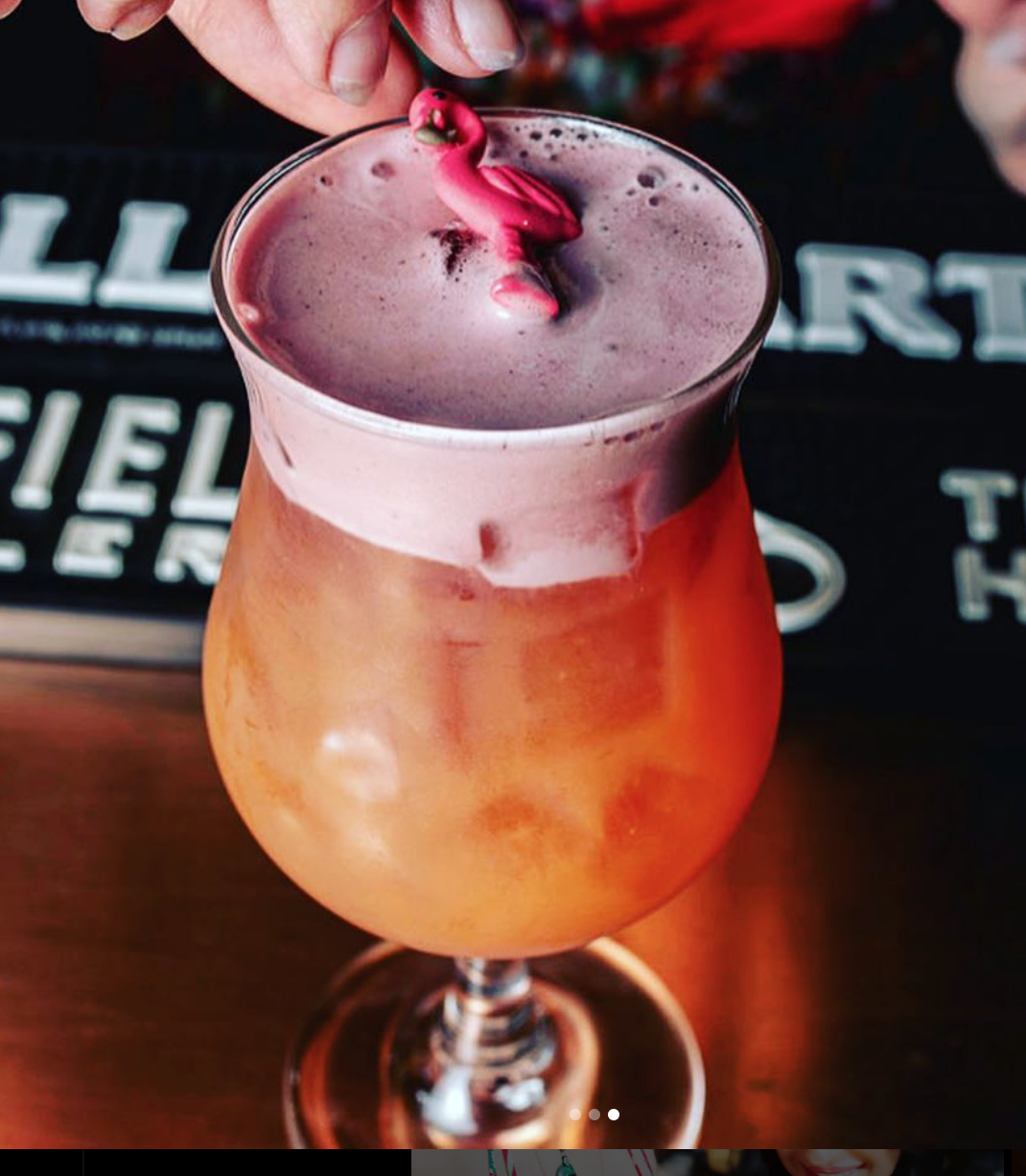 A tropical cocktail in a hurricane glass topped with pink foam and garnished with a plastic flamingo stirrer.