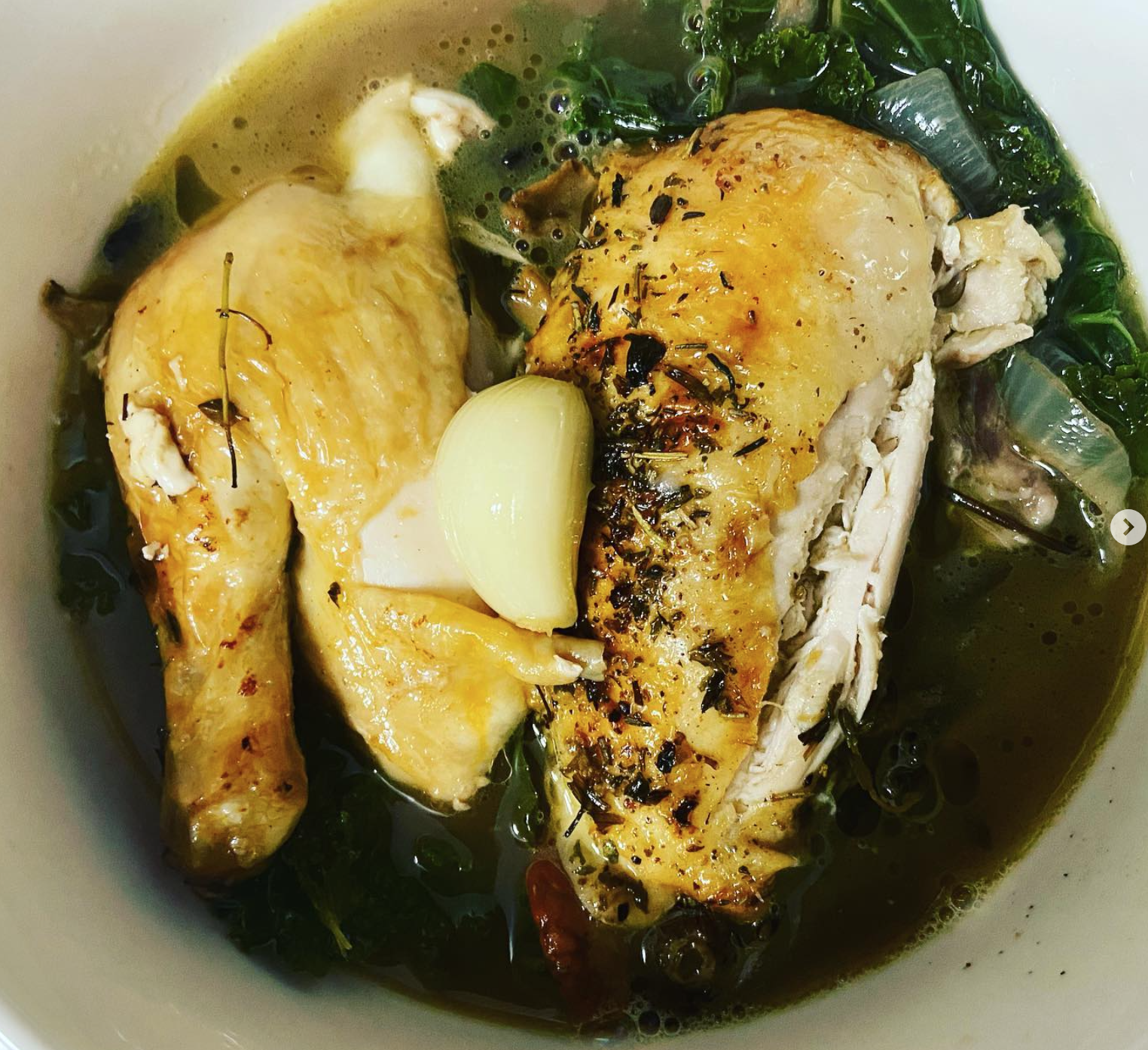 Cooked chicken leg with garlic and herbs, served in a broth with greens.