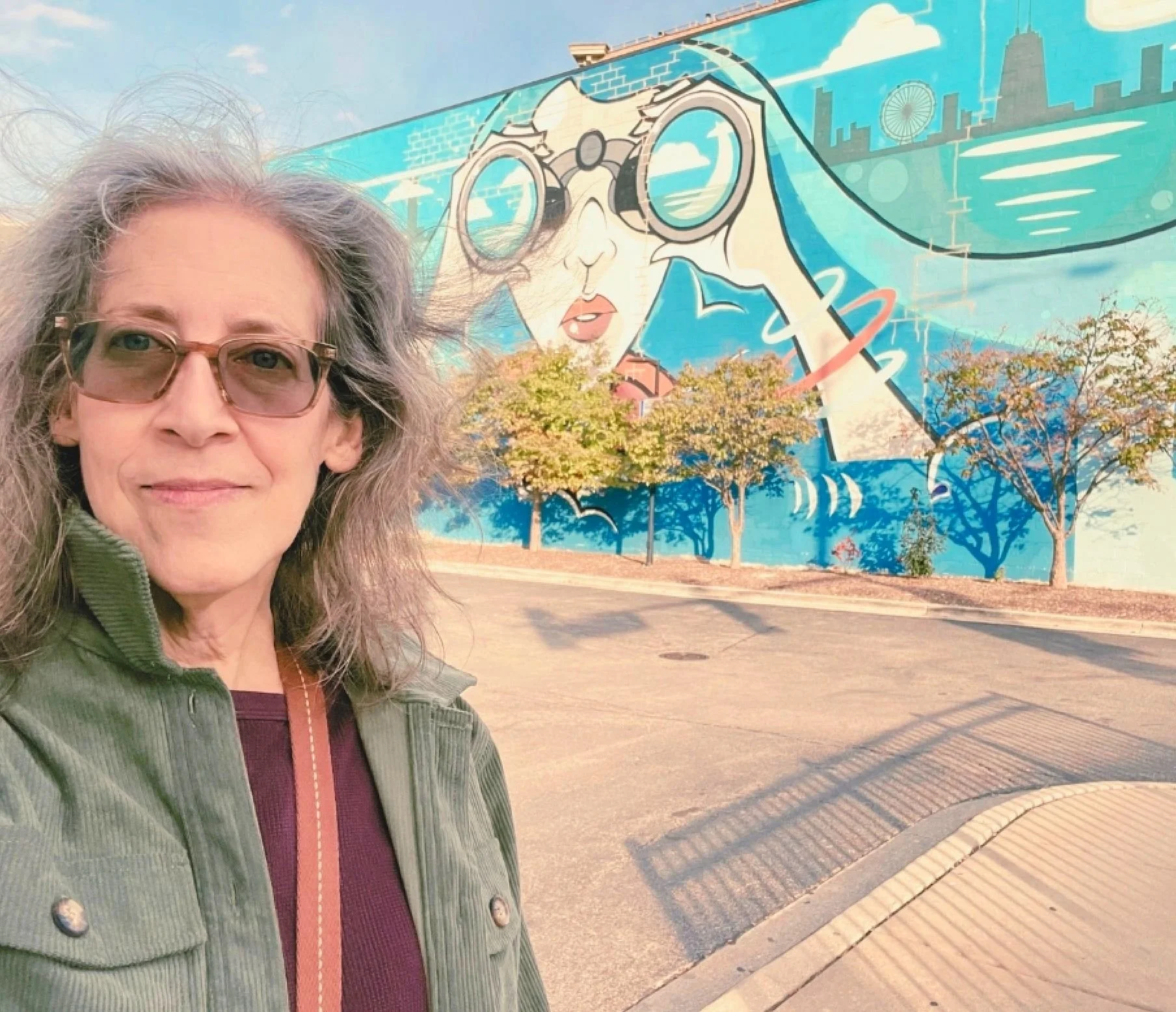 Woman taking a selfie in front of a colorful mural depicting a cityscape and a person with binoculars.