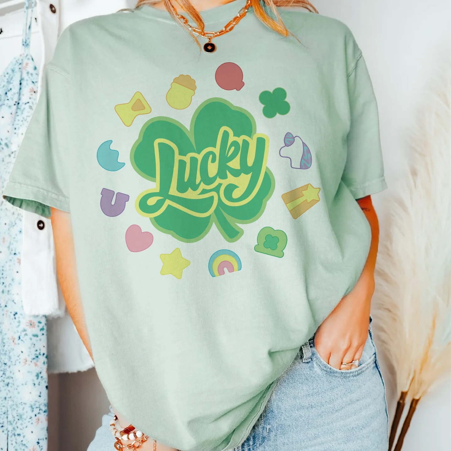 Person wearing a light green oversized T-shirt with a shamrock and the word "Lucky" in the center, surrounded by colorful small icons like hearts, stars, rainbows, and other shapes.