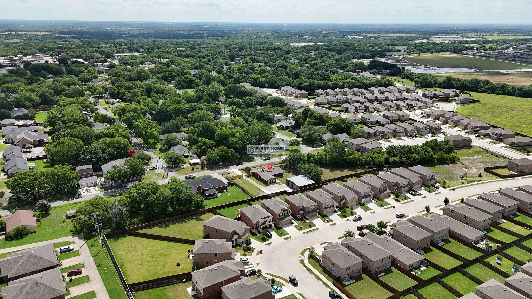 Aerial view of a suburban neighborhood with houses, trees, and roads, showing a mix of single-family homes and community layouts.