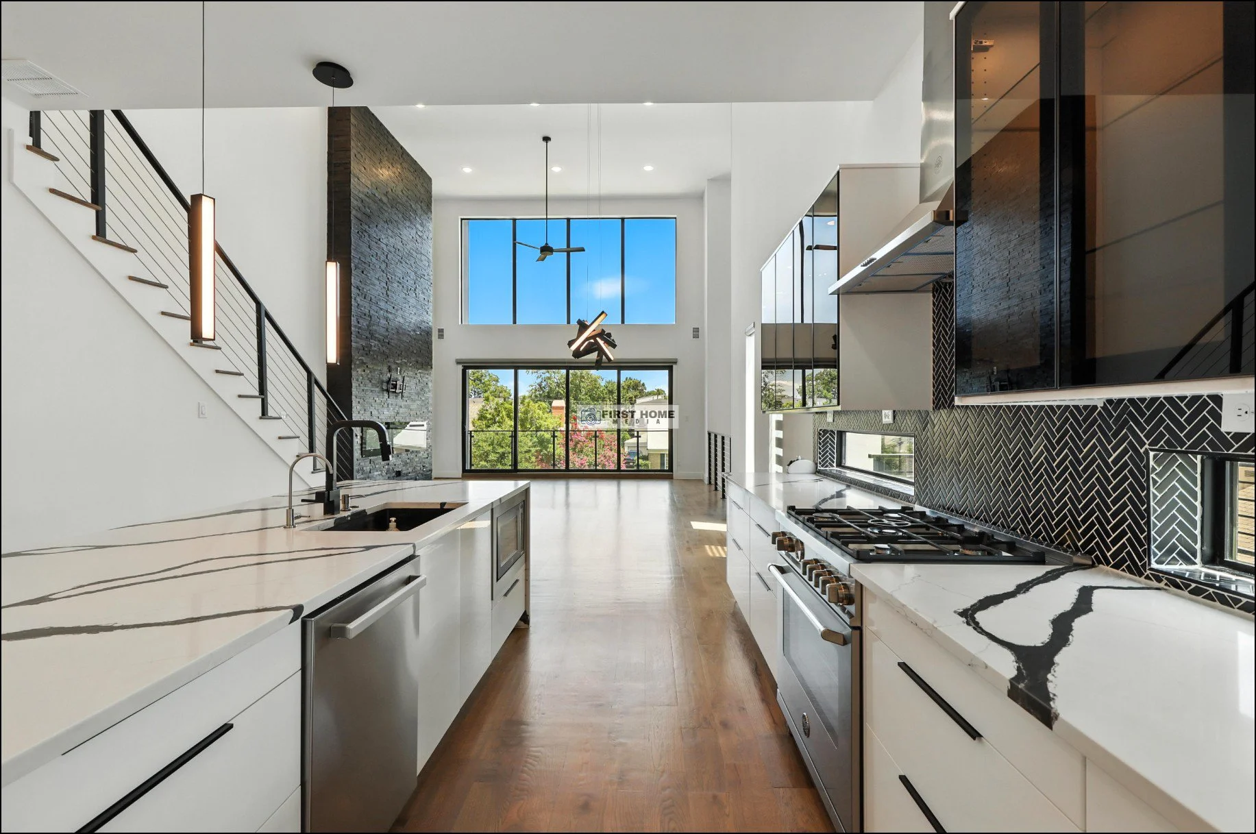 Modern kitchen with white cabinets, black accents, marble countertops, and large windows with a view of trees.