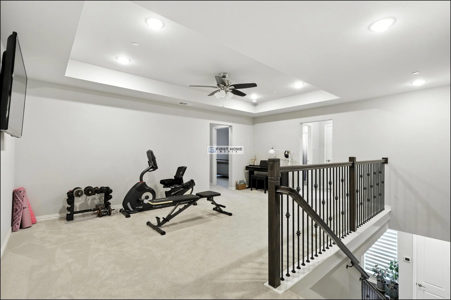 Upper level in a home with exercise equipment, a black upright piano, and a staircase railing, with a white ceiling and walls, and recessed lighting.