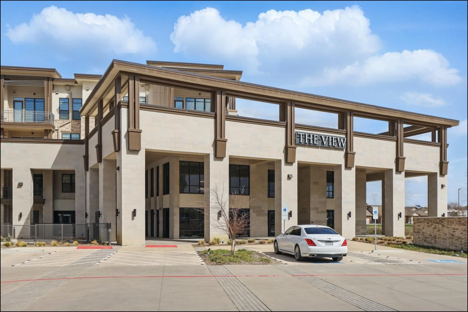 Modern apartment building labeled 'The View' with beige stone exterior, large windows, and a car parked in front.